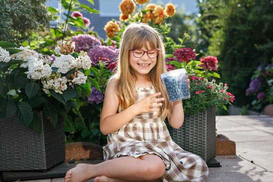 Little schoolgirl with glasses picking and eating fresh ripe blueberries in summer. Happy child enjoying nature. Real life, real people.