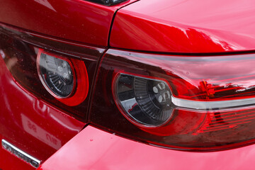 Red car rear light closeup showing glossy painted metal and chrome trim, reflective surface and water droplets giving moody automotive detail © CoreRock
