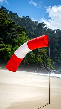 A red and white windsock on a beach with trees
