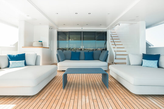 Modern Superyacht interior, aft deck lounge, with teak deck, ample loungers for guests to enjoy the sea view, with decorative pillows 