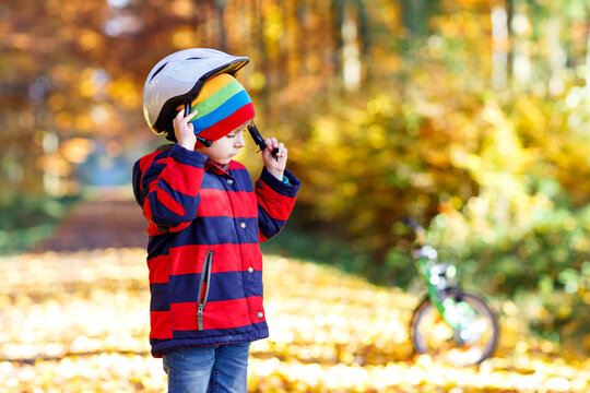 Active child putting safe helmet before cycling on sunny fall day in nature.