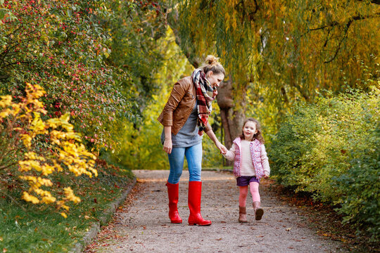Mother and daughter walking in autumn park together. Happy family enjoying fall season outdoors. Real life, real people