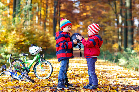 Two little kid boys with bicycles in autumn forest putting helmets