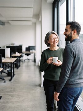 Zwei l&auml;chelnde Kollegen bei der Kaffeepause am Fenster im modernen B&uuml;ro &uuml;ber die Schulter fotografiert