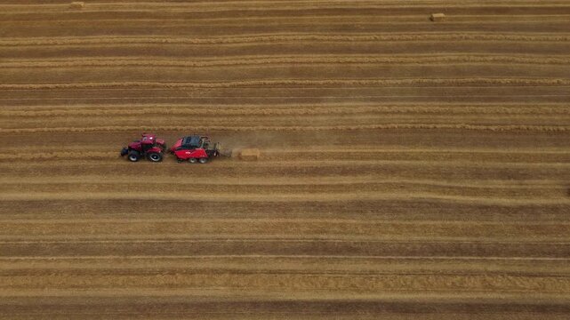 Aerial view of red square baler machinery baling straw on farmland after harvest
