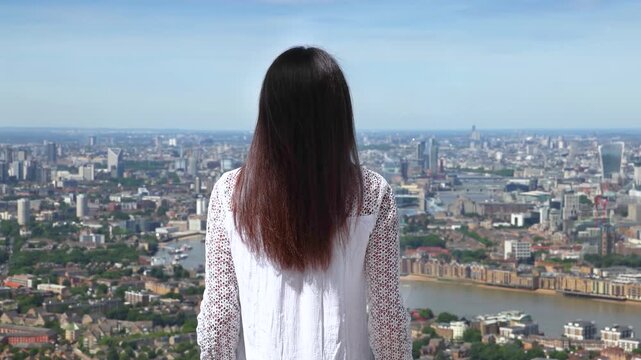 A woman looks at the panoramic, elevated view of the skyline of London, England, during a sunny summer day