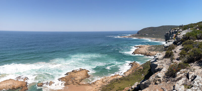 High resolution stitched panorama of Robberg Nature Reserve, South Africa, featuring a wide angle panoramic view of rocky ocean cliffs, crashing turquoise waves, and a rugged wilderness coastline.