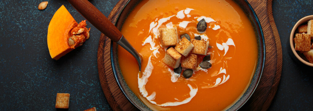 Pumpkin soup croutons cream fresh pumpkin slices wooden board dark background autumn winter