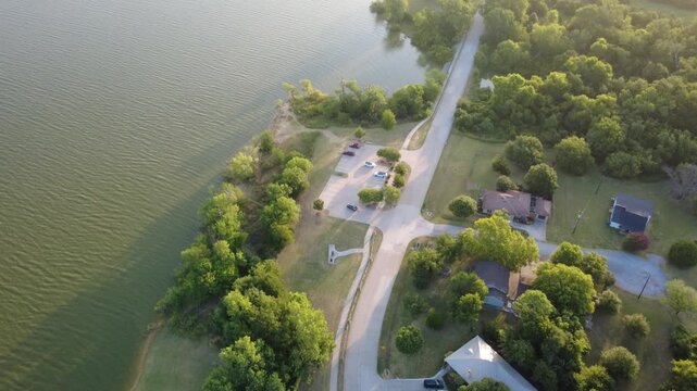 Winding subdivision tarmac connects residential cul de sacs bordering lush shoreline foliage by Lewisville Lake within Lakewood Estates. Suburban growth dynamics highlight within Little Elm, DFW