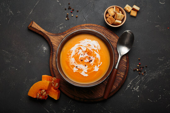 Pumpkin soup croutons cream fresh pumpkin slices wooden board dark background autumn winter