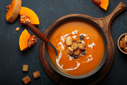 Pumpkin soup croutons cream fresh pumpkin slices wooden board dark background autumn winter
