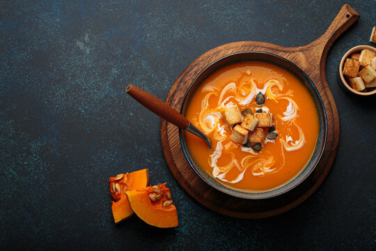 Pumpkin soup croutons cream fresh pumpkin slices wooden board dark background autumn winter copy