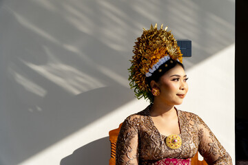 Side profile portrait of a Balinese woman in traditional golden crown and kebaya with natural leaf shadows © IgnasiusIMade
