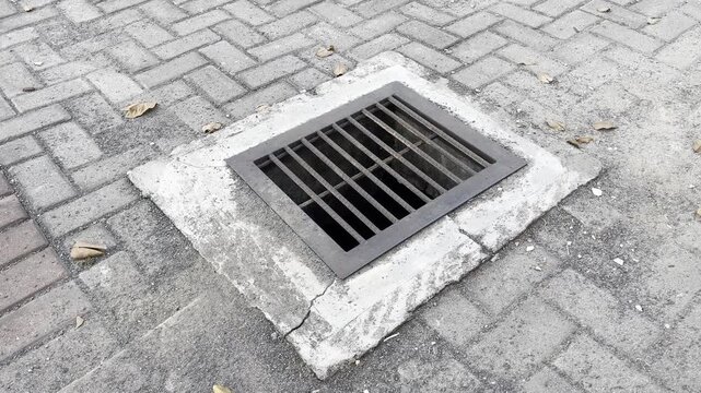 Square iron drainage grate inlet on weathered interlocking paving blocks