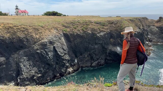 A mature woman enjoys a hike on a coastal trail with views of the Pacific Ocean and Cabrillo Lighthouse in Mendocino California