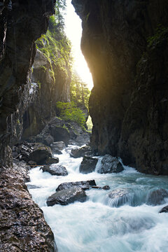Stunning narrow gorge with sunbeams filtering between rocky cliffs and rushing water. Partnach Gorge in the Bavarian Alps, Germany