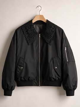 A black bomber jacket with a distinctive lace collar is displayed on a wooden hanger against a plain white background, highlighting its design and texture.