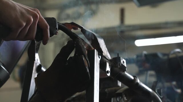 An engineer welds a frame, gear sprocket, and chassis for a homemade scooter/snowmobile with a small trailer.