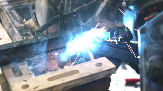 An engineer welds a frame, gear sprocket, and chassis for a homemade scooter/snowmobile with a small trailer.