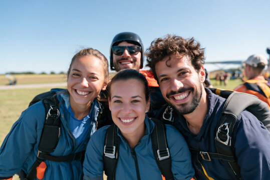 Group of friends preparing for first parachute jump at drop zone, smiling faces, outdoor adventure concept.