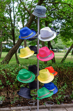 Various colorful hats display on a metallic rack outdoors in a green park environment.