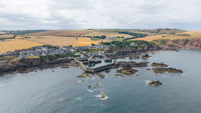 Scenic panoramic landscape of St Abbs village with its historic fishing harbor, pier, rugged rocky coastline, and North Sea shore in Berwickshire, Scotland