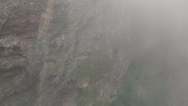 A static shot captures the dramatic, fog-shrouded mountain cliffs of "Las Ventanas de G&uuml;&iacute;mar" on Tenerife. A narrow path through tunnels is carved into the and rocky landscape.