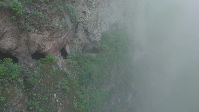 A drone pushes in on the rugged, green cliffs of "Las Ventanas de G&uuml;&iacute;mar" on Tenerife, revealing old water tunnels in the mountaim, shrouded in thick fog. A remote and mysterious island landscape.