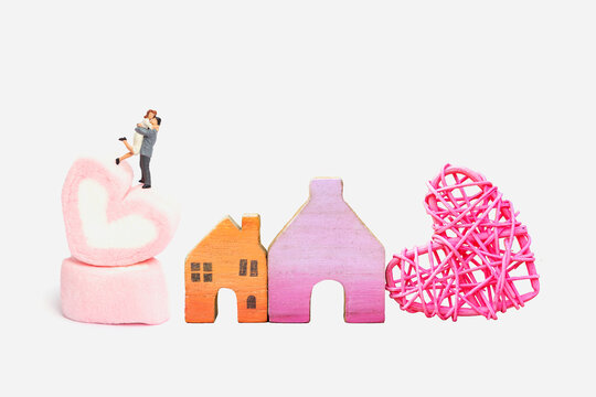 Miniature couple on pink heart with house model isolate on white background, valentine celebration, love and romance, real estate industry
