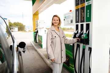 Obraz premium Woman smiling and holding a fuel pump nozzle, getting fuel for her car