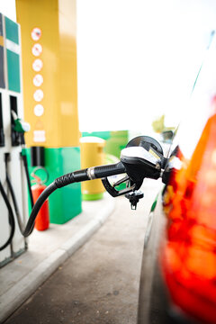 Refueling a red car at a gas station, focusing on the nozzle and pump
