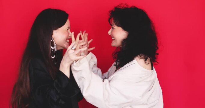 Two excited Caucasian women screaming with joy celebrating victory holding hands and laughing together on bright red studio background, winning success concept stock video clip