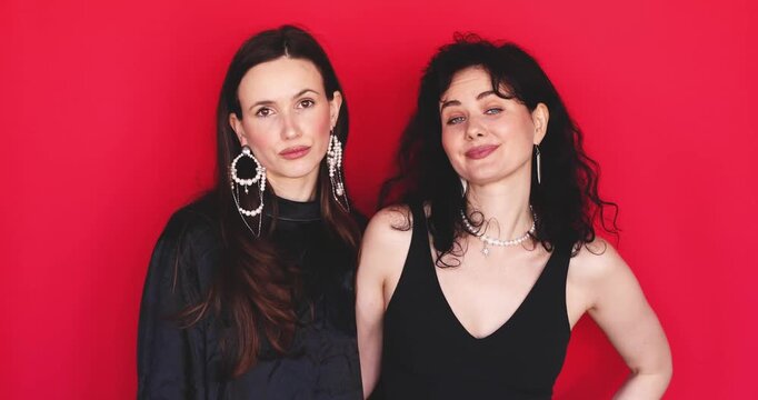 Two attractive Caucasian women standing together shaking head no gesturing refusal with calm expressive faces looking at camera on bright red studio background, saying no disagreement stock video clip