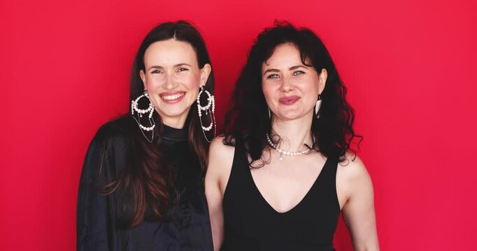 Two attractive Caucasian women standing together nodding heads yes gesturing agreement with smiling friendly faces looking at camera on bright red studio background, approving concept stock video clip