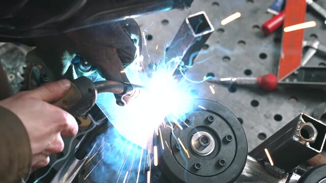 An engineer welds a frame, gear sprocket, and chassis for a homemade scooter/snowmobile with a small trailer.
