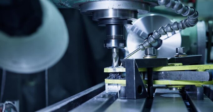 Slow motion milling machine drill cutting metal workpiece in industrial workshop, tracking static shot.