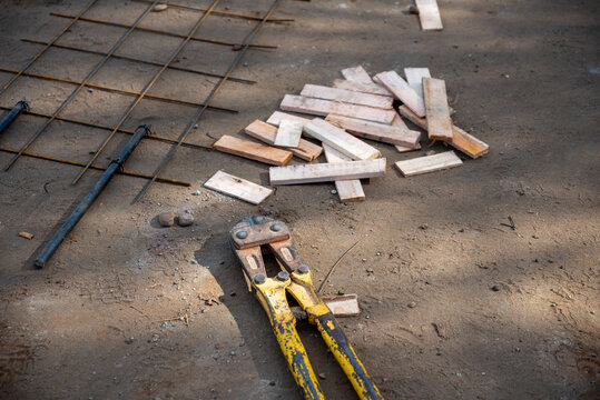 Yellow bolt cutter, rebar steel mesh, and wooden spacers on ground at construction site