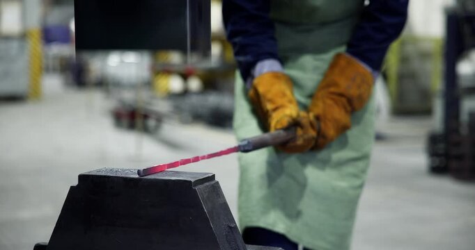 Blacksmith forging glowing hot metal on anvil in industrial workshop with closeup steady pan movement.
