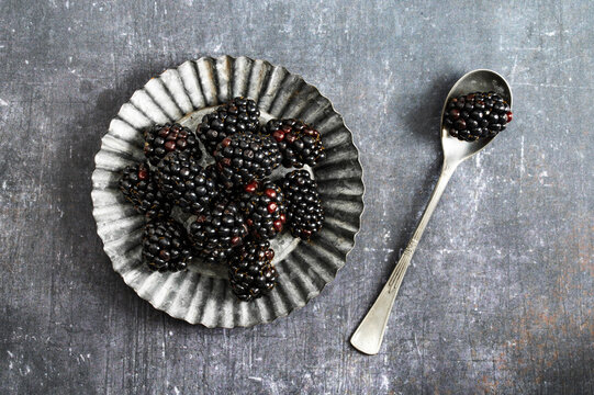 Fresh organic blackberries in a small metal plate and a spoon on dark rustic background