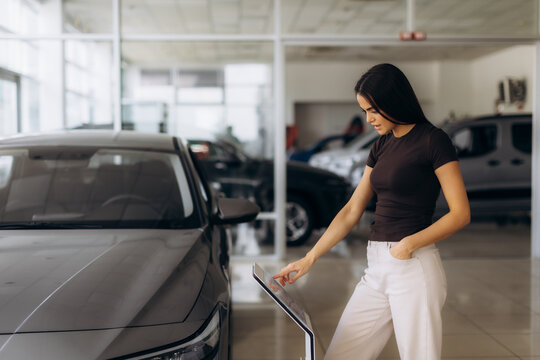 Woman customer choosing new car at modern showroom