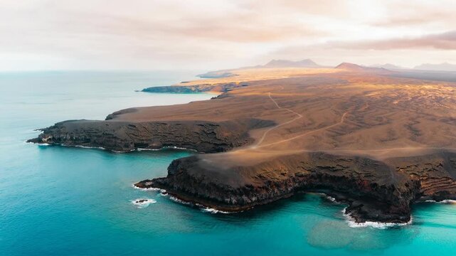 Aerial view of volcanic coastline with rugged cliffs and turquoise ocean under soft cloudy sky