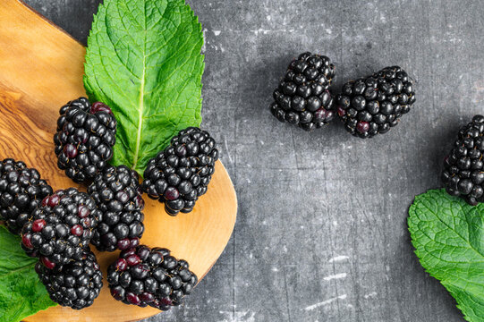 Fresh blackberries with mint leaves on a wooden board and dark background