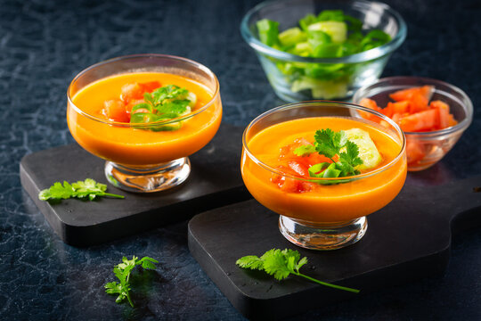 Vibrant orange gazpacho soup garnished with fresh herbs and vegetables
