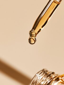 Cosmetic pipette with golden serum drop. Skincare oil dripping from glass dropper.