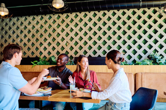 Diverse friends sharing a meal and engaging in lively conversation at a modern restaurant, depicting social gathering and dining