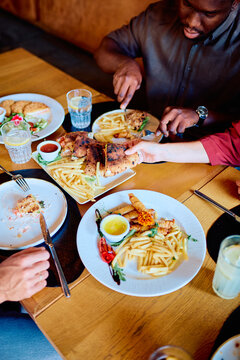 People eating various dishes and appetizers, including french fries, calzone, and drinks, from shared plates on a wooden table