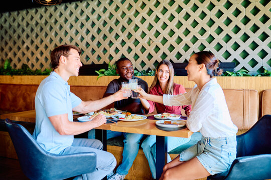 Diverse friends enjoying a meal and toasting drinks, celebrating special moments at a modern restaurant. Sharing happiness