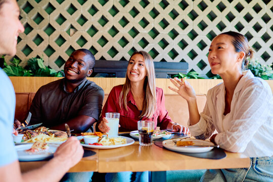 Diverse group of friends dining together at a restaurant, eating and having a lively conversation. Focus on friendship and connection