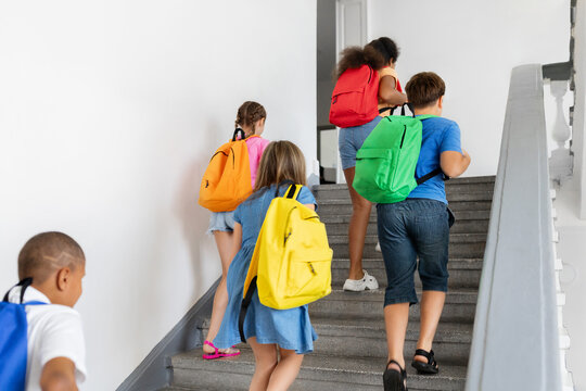Diverse schoolchildren with colorful backpacks walking upstairs together inside school building, representing daily campus routine, friendship, movement, and student life