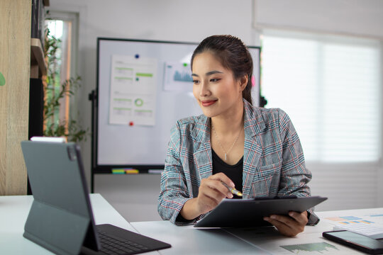 Asian businesswoman working with tablet and taking notes in modern office.